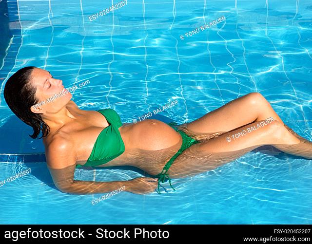 Beautiful pregnant woman sun tanning at blue pool