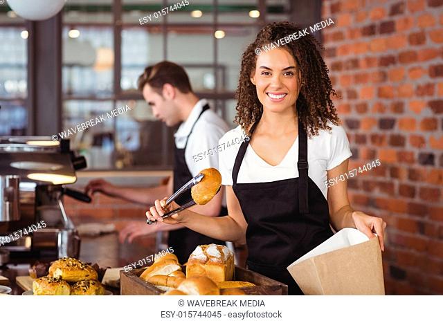 Smiling waitress putting bread roll in paper bag
