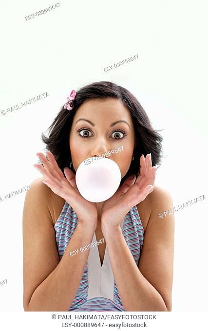 Beautiful Latina girl with huge eyes open blowing a bubblegum bubble, isolated