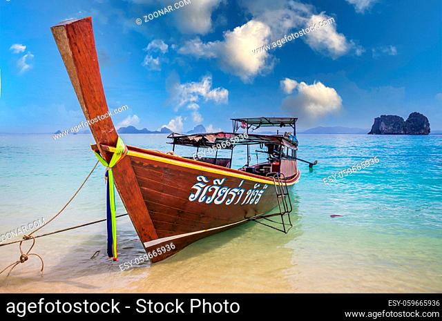 Longtail boat in crystal clear blue waters under blue sky waiting for passengers on beautiful white beach in Ko Mok, Thailand