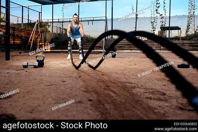 Strong man doing exercise with ropes, street workout, crossfit. Fitness training on sports ground outdoor, male person pumps muscles, active urban lifestyle