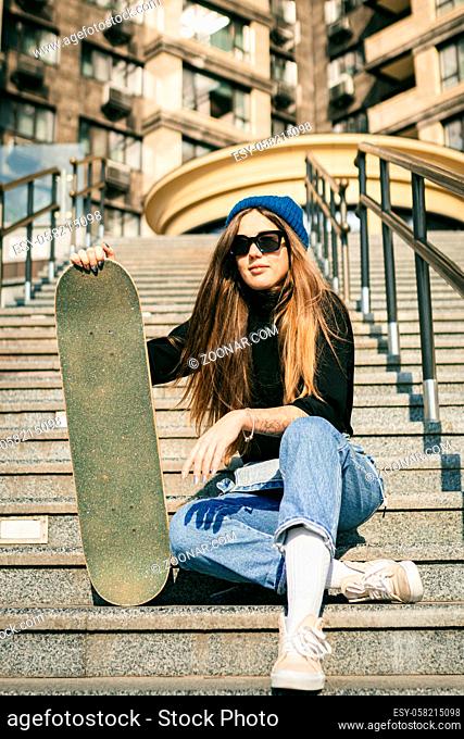 Urban woman with skate. Hipster girl with skateboard in city. Extreme sport and emotions concept. Alternative lifestyle. Stylish hipster girl holding skateboard...