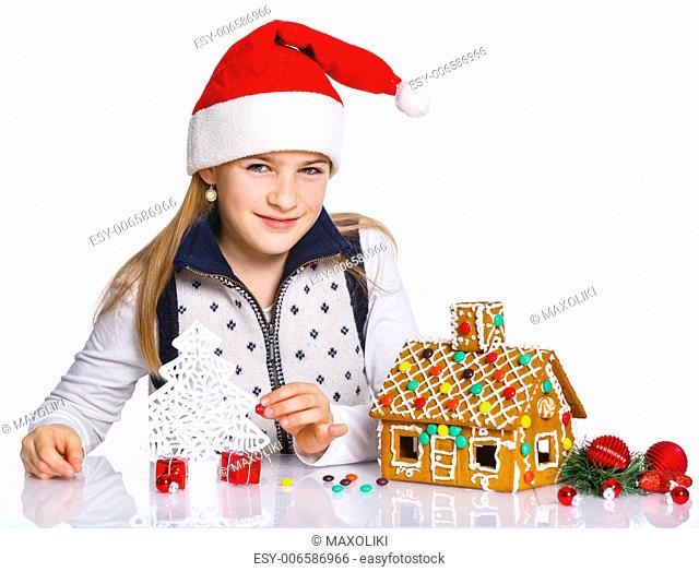 Christmas theme - Smiling girl in Santa's hat with gingerbread house, isolated on white