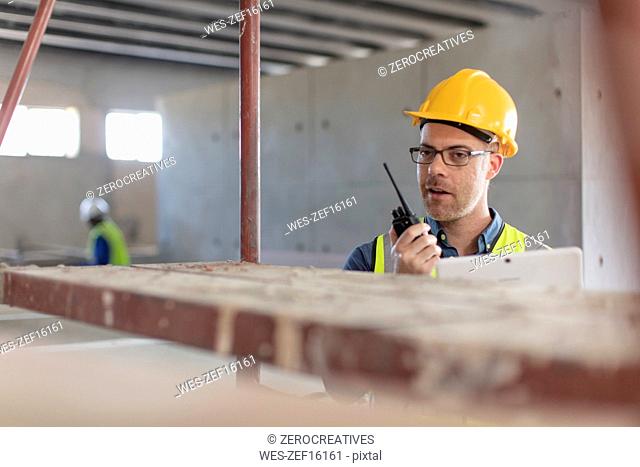 Architect using walkie talkie and laptop at construction site