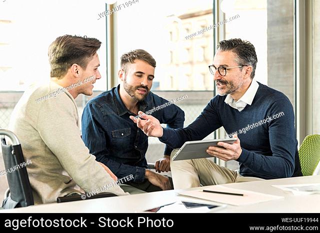 Three businessmen having a meeting in office sharing a tablet