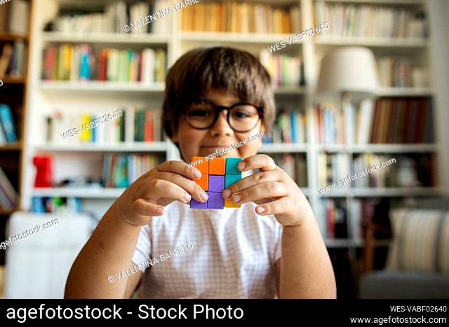 Smiling little boy holding cube made of building blocks