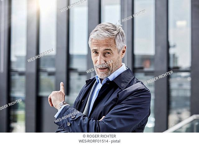 Germany, Duesseldorf, portrait of businessman pointing at office building at Media Harbour