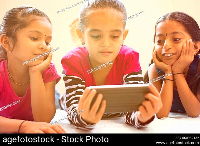 Three cute Indian children watching child using smartphone with smiley faces on bed