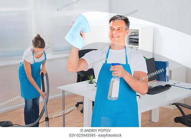 Male Worker Cleaning Glass With Rag While Female Worker Vacuuming Floor