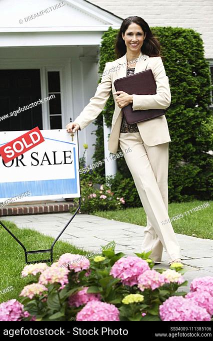 Hispanic female real estate agent and Sold sign in front of house