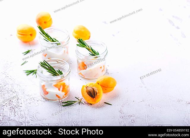 Natural yogurt with pieces of apricots, Walnut and rosemary in mini glass jars on light background
