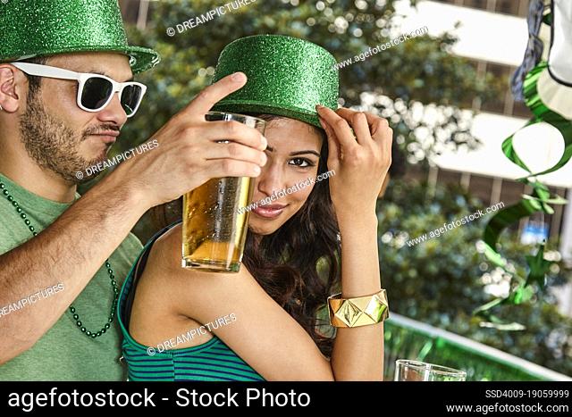 Man and woman wearing green sparkle hats dancing while holding beer bottles for St. Patrick's Day Party