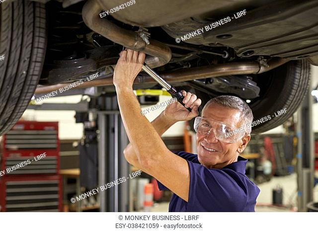 Portrait Of Auto Mechanic Working Underneath Car In Garage