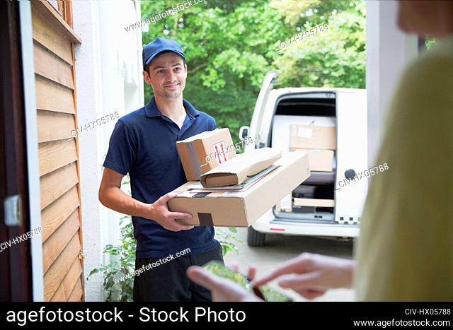 Smiling deliveryman watching woman signing smart phone at front door