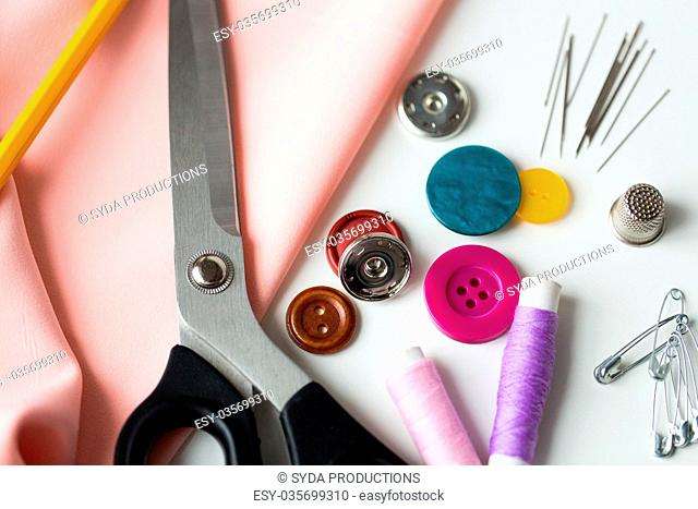 needlework and tailoring concept - scissors, sewing buttons, spools of thread, needles and cloth