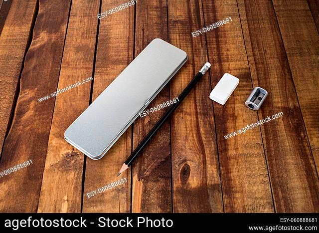 Metal pencil case, pencil, sharpener, eraser on wooden background. Blank stationery template
