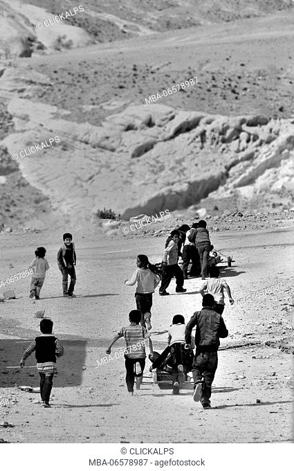 In a road on the outskirts of Petra, some children playing and chasing each other on a dirt road and dusty
