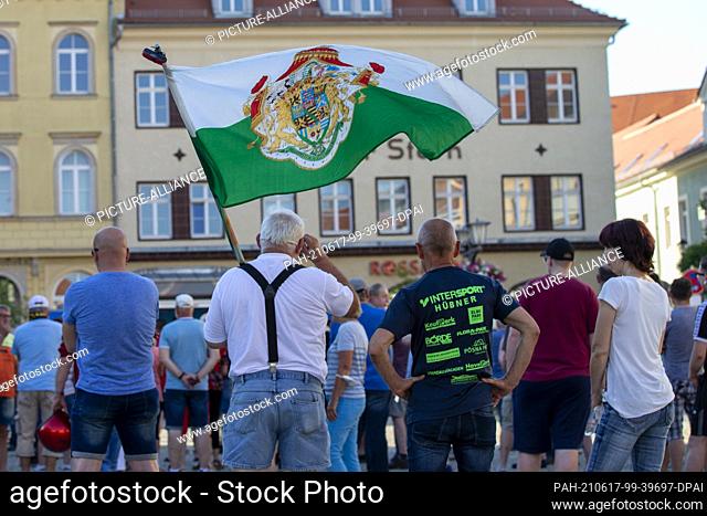 17 June 2021, Saxony, Kamenz: A man with a flag (M.) stands on the market square in Kamenz during a rally of the AfD. At the rally of the AfD district...
