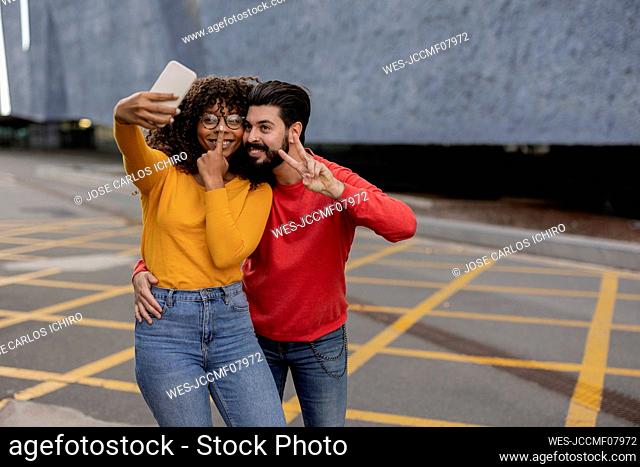 Happy young couple taking selfie through smart phone at footpath