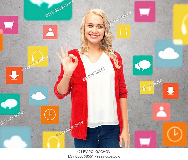 gesture, multimedia and people concept - happy smiling young woman in red cardigan showing ok hand sign over gray background with menu icons