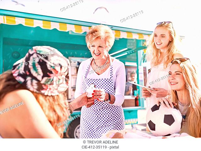 Senior female business owner serving ice cream to young women outside sunny food cart