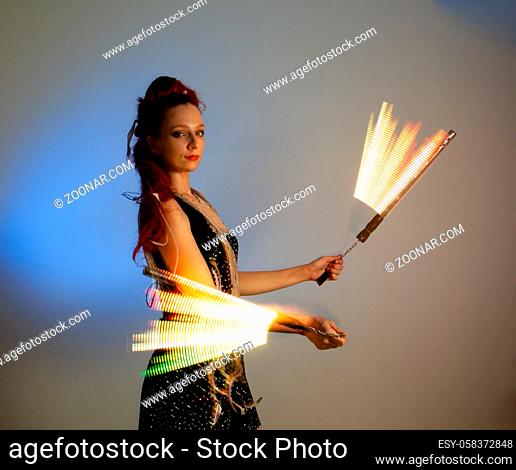 Sideview female dancer with fire show props in motion. Effective light show with fire show props. Beautiful woman in costume posing on light background