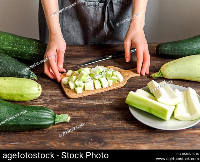 Zucchini harvest. Woman slices zucchini cubes for freezing on wooden table. Farm organic zucchini harvesting