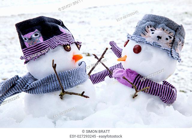 Two cute snowmen dressed for winter in scarfs and hats embracing each other as long lost friends. Winter scene with snow