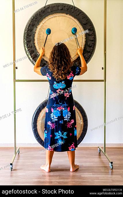 Female sound therapist playing gong while standing in studio