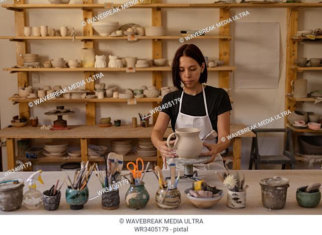 Front view of a young Caucasian female potter standing at a work table holding a jug on a banding wheel in a pottery studio