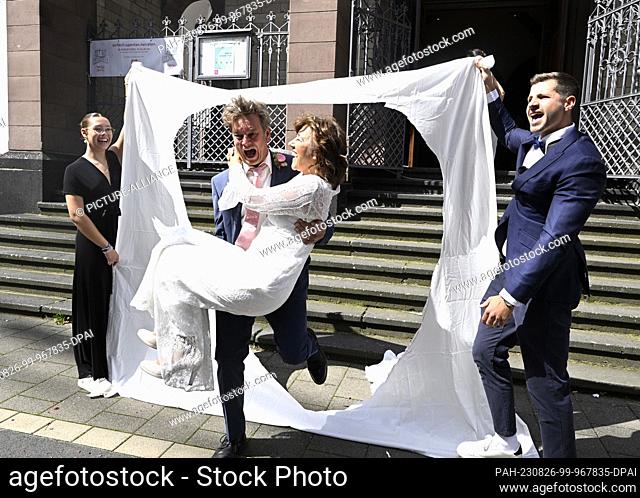 26 August 2023, North Rhine-Westphalia, Cologne: Kaja (l) carries Diana (r) through a fabric heart she cut out herself in front of Christ Church after her...