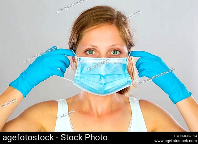 Blond woman wearing Blue face mask with white background. Young female covering mouth with surgical mask in studio. Model putting on respiratory with blue latex...