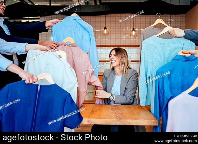 Young contemporary stylist looking through set of shirts and other casualwear choosing one for fashion shooting
