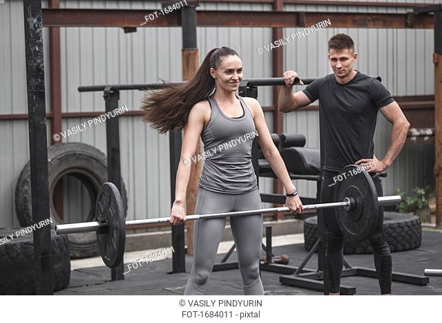 Male instructor looking at female athlete smiling while lifting barbell during cross training
