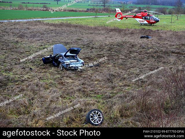 02 January 2021, Lower Saxony, Göttingen: A car lies far off the road after an accident, with a rescue helicopter in the background