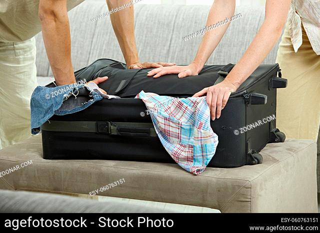 Hands trying to close full suitcase, pressing down
