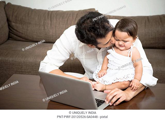 Man using a laptop and kissing his daughter sitting with him