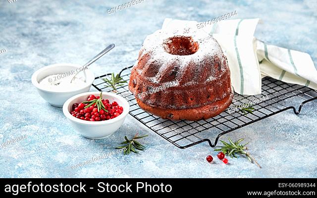 Chocolate cake sprinkled with powdered sugar on a metal wire rack, powdered sugar and cranberries in bowls, prepared for decoration