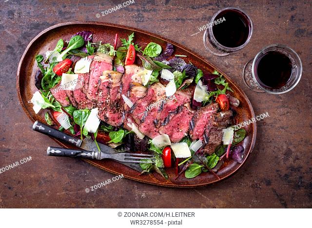 Traditional Italian Tagliata Steak with Parmesan and Salad as close-up on a plate