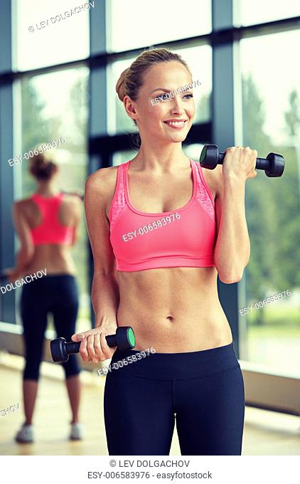 sport, fitness, training, weightlifting and people concept - young sporty woman with dumbbells flexing biceps in gym