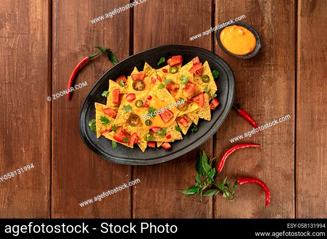 A platter of nachos, Mexican tortilla chips, shot from the top with a cheese sauce, chilli and jalapeno peppers, tomatoes