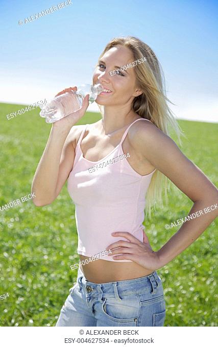Junge Frau im Frühling oder Sommer trinkt Wasser aus der Flasche