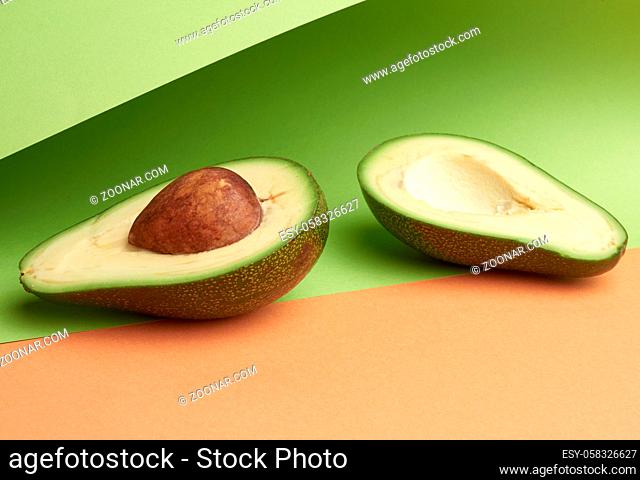half ripe green avocado with a brown bone on an abstract green-orange background with curved paper