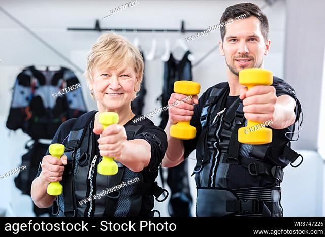 Fit senior lady and young man in ems gym exercising with dumbbells
