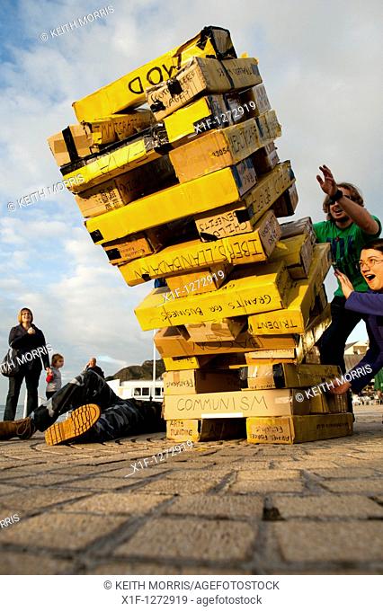 Aberystwyth University student street theatre group 'Explodingfish' playing a game of giant Jenga to highlight the government's spending cuts and the choices...