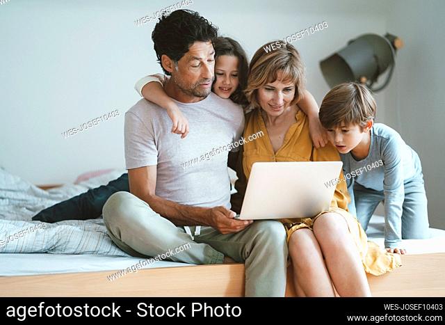 Family sharing laptop sitting on bed at home
