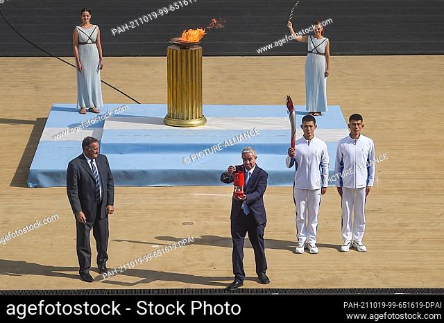 19 October 2021, Greece, Athen: Yu Zaiqing (r), vice president of the Chinese Olympic Committee, holds the Olympic Flame during the ceremony to hand over the...