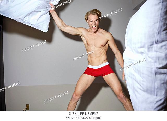 Portrait of screaming man in bedroom throwing pillows