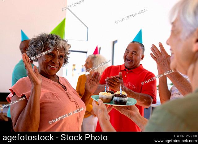 Cheerful multiracial seniors clapping and singing for senior woman while celebrating birthday