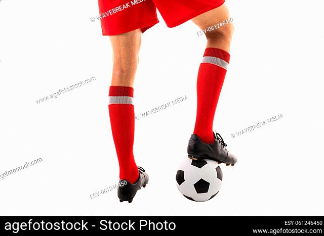 Low section of young male caucasian athlete stepping on soccer ball against white background